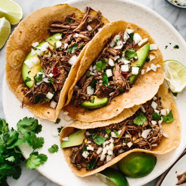 Barbacoa tacos next to cilantro, lime, and tortillas.