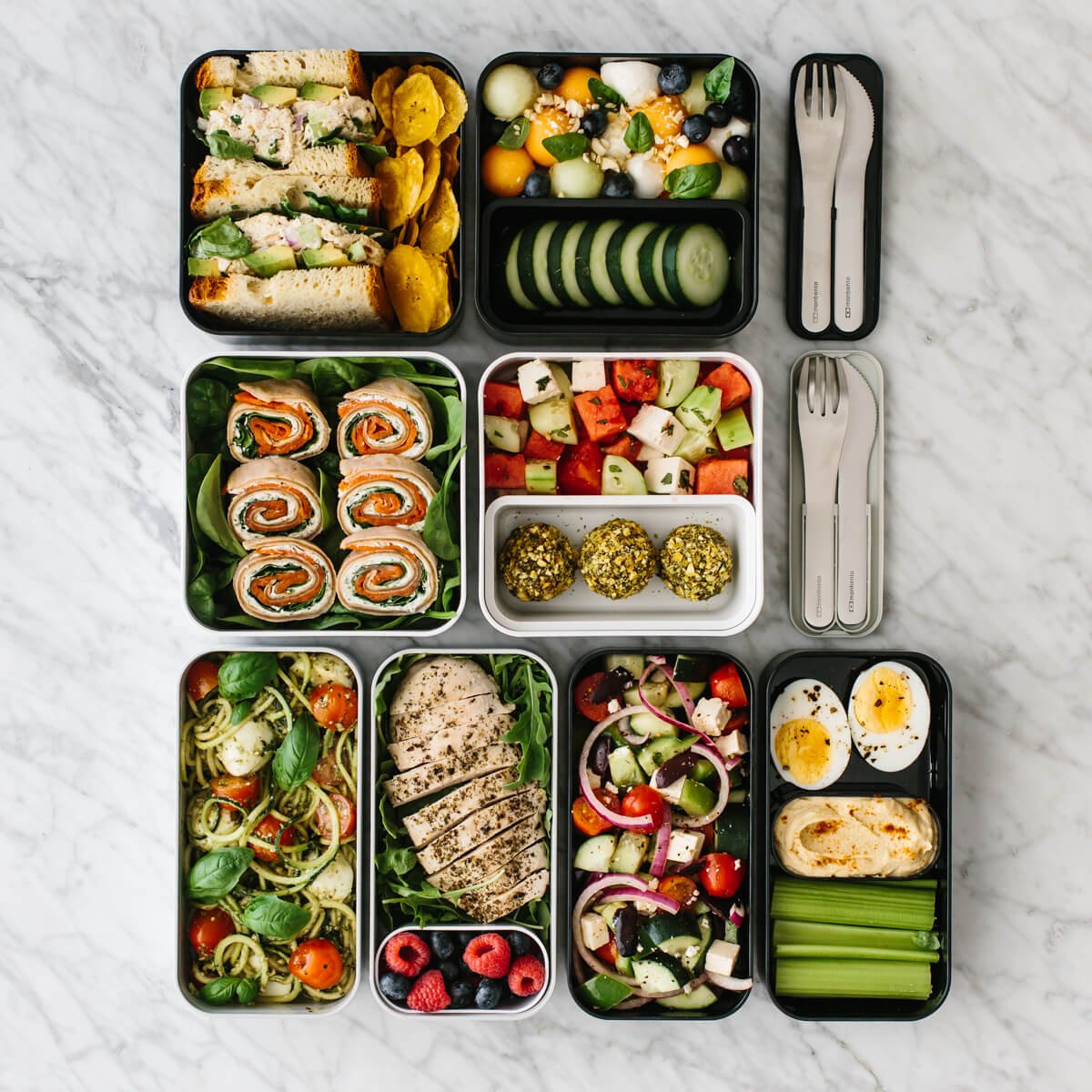 Several bento box lunches on a counter with cutlery.