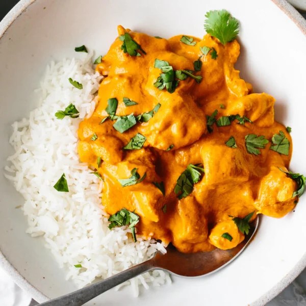 A bowl with butter chicken and rice with a spoon