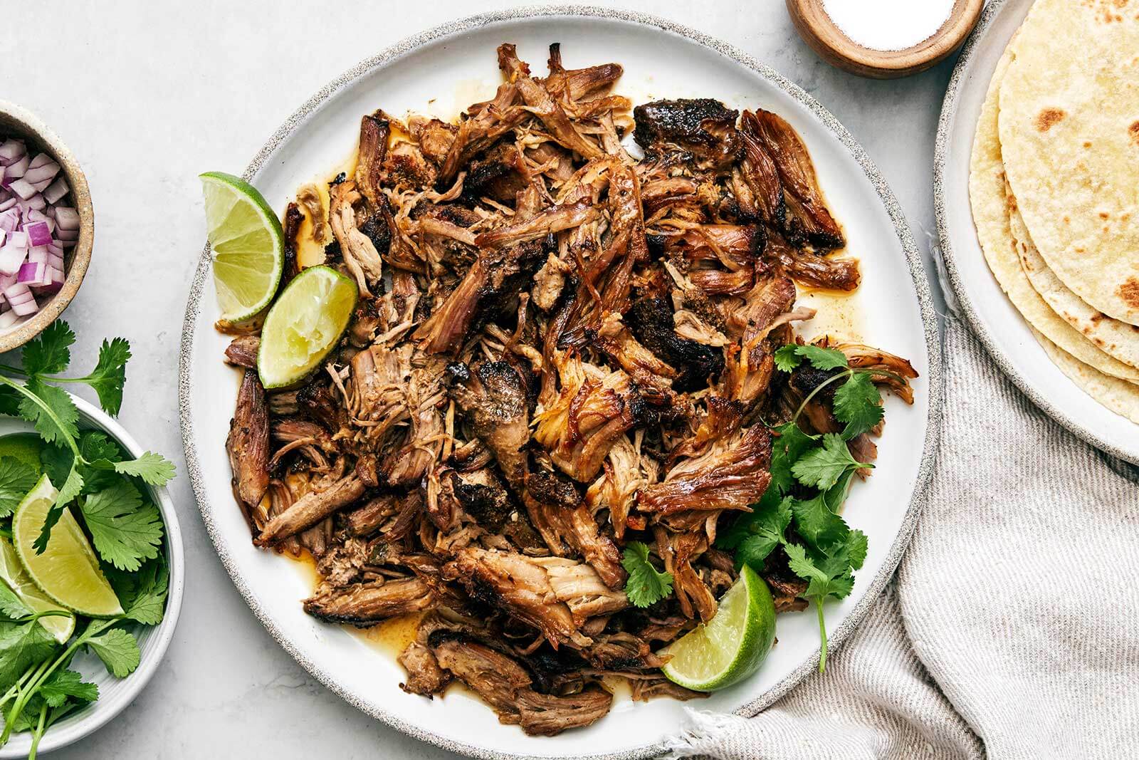 Carnitas on a plate next to tortillas.