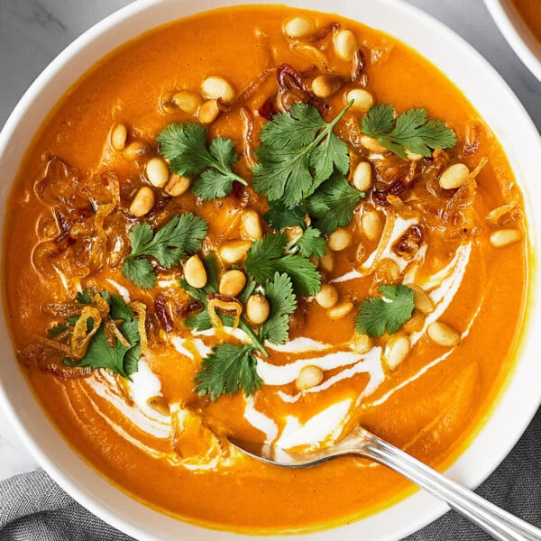 A white bowl of carrot ginger soup next to a napkin