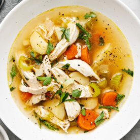 A bowl of chicken soup next to spoons.