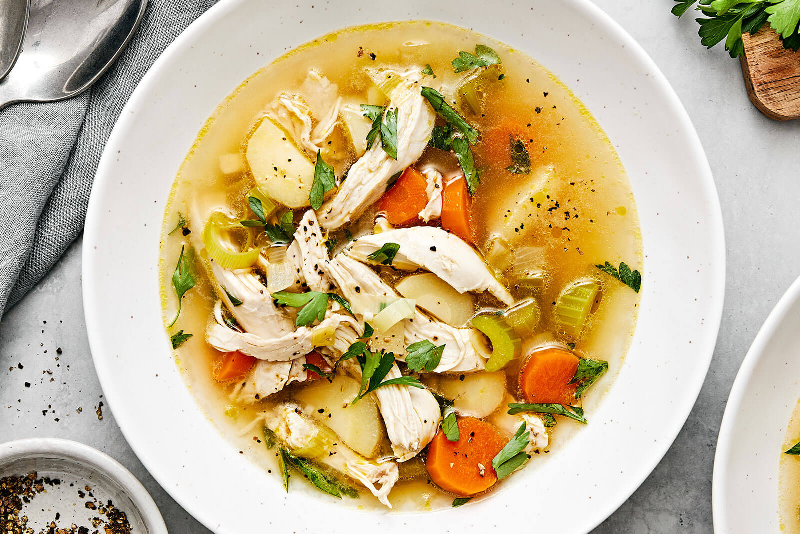 A bowl of chicken soup next to spoons.