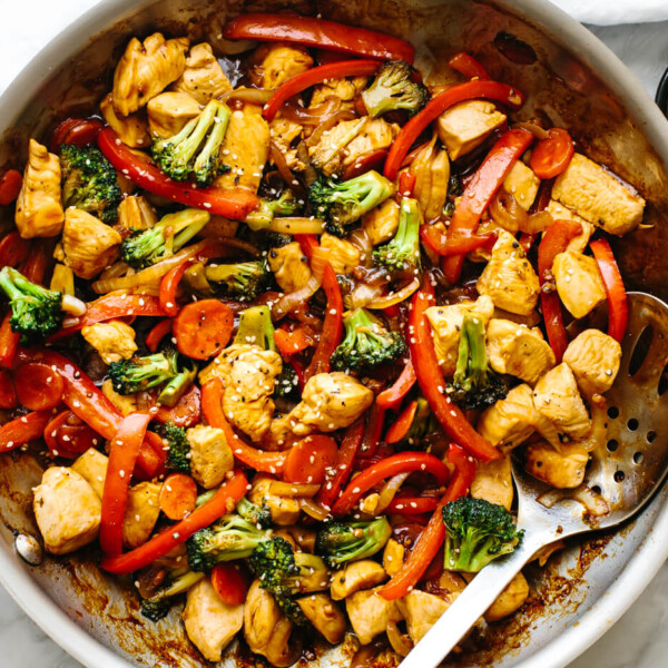 Chicken stir-fry in a pan next to sesame seeds.