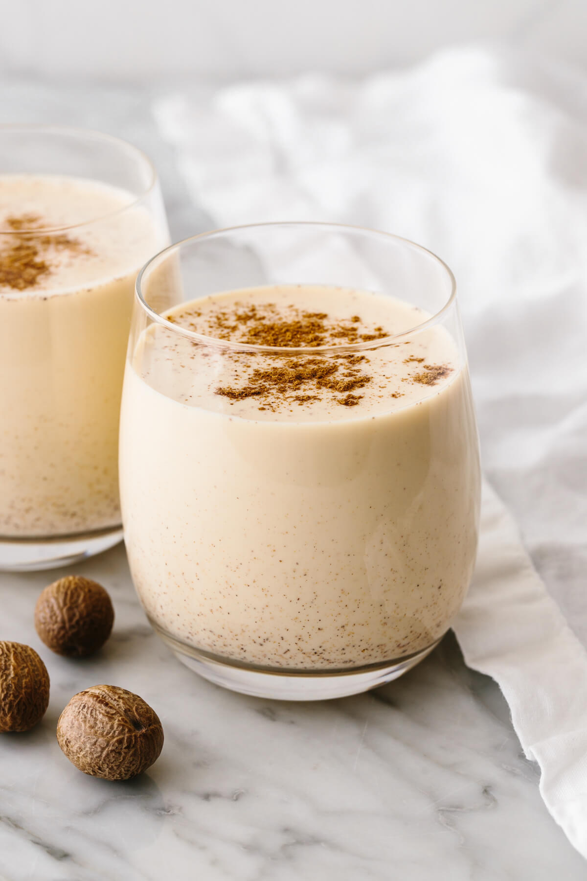 Homemade eggnog in 2 glasses on a table with a napkin.