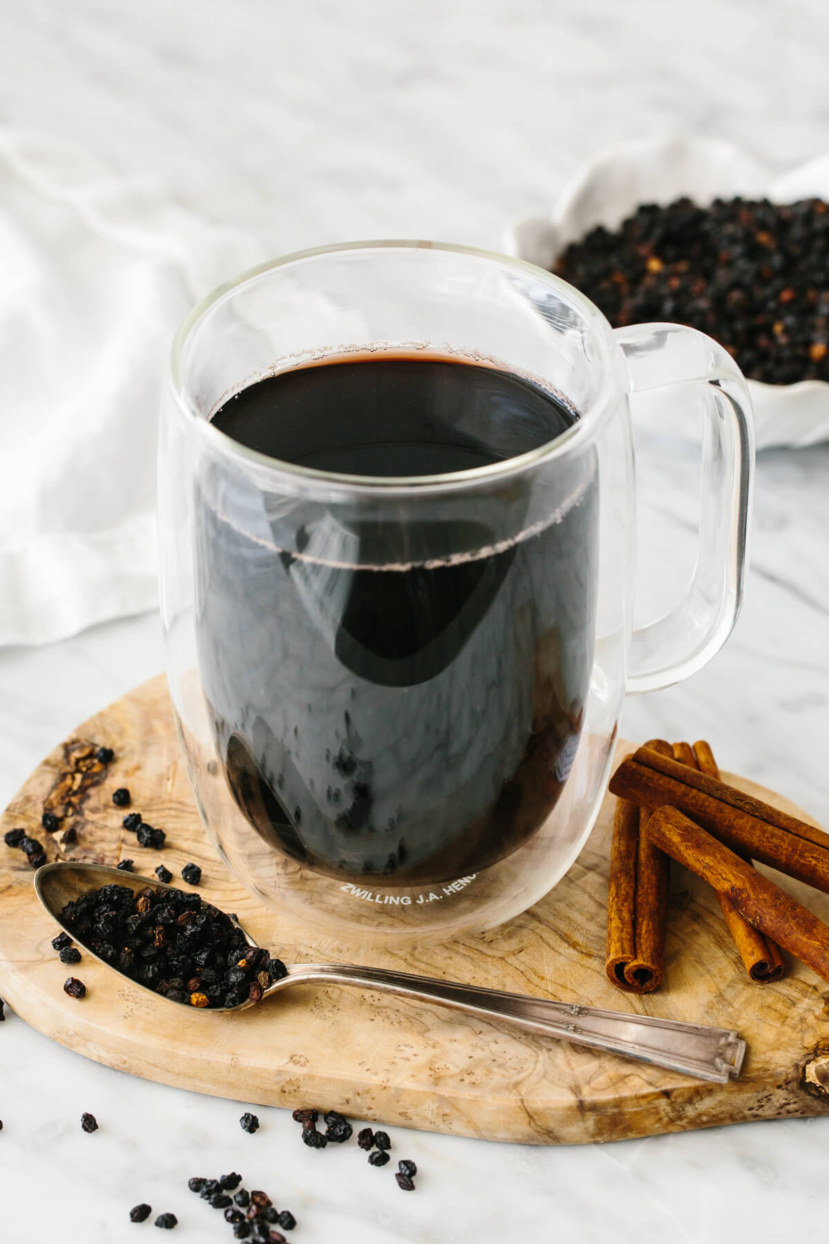 Elderberry tea in a glass next to dried elderberry and cinnamon sticks.