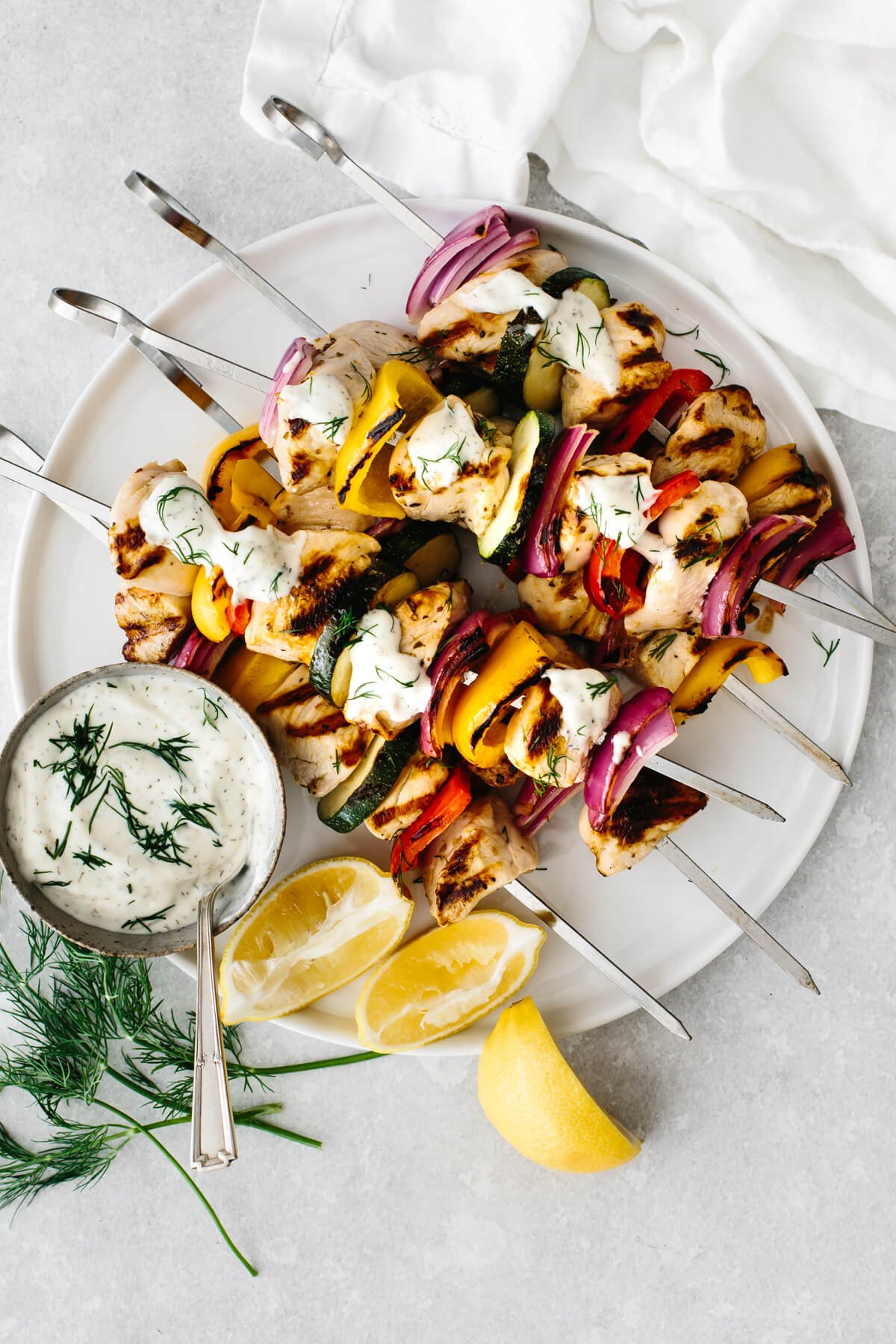 Greek chicken kabobs on a white plate with tzatziki sauce.