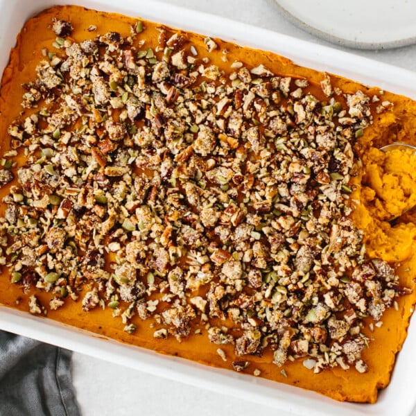 Mashed sweet potato topped with a pecan crumble in a white casserole dish.