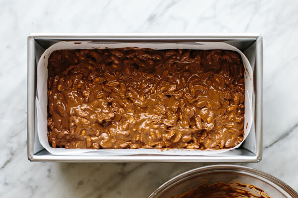 Pouring chocolate crunch bar mixture into a loaf pan.