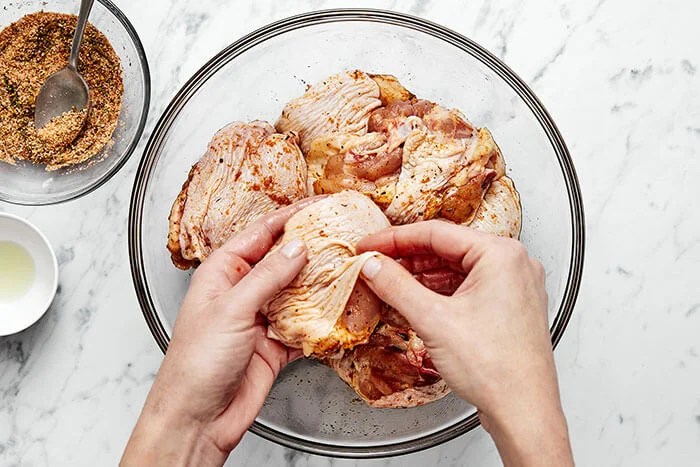 Seasoning chicken with hands.