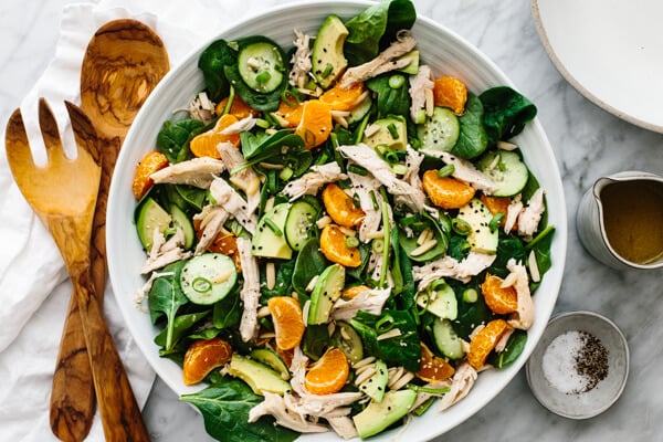 A bowl of mandarin chicken salad next to serving spoons.