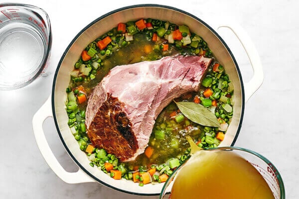 Pouring broth into a pot of split pea soup