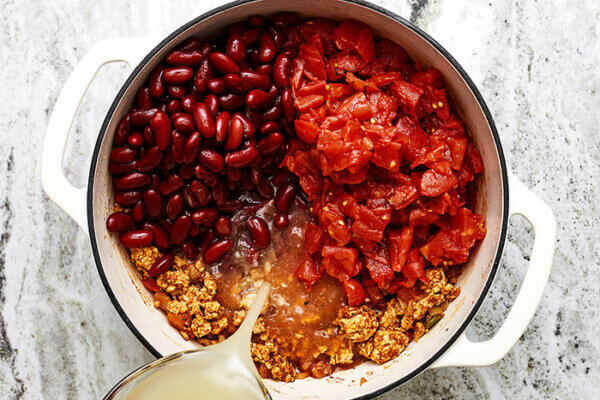 Pouring broth into a pot of turkey chili