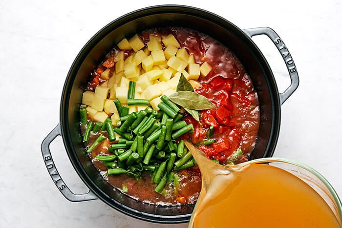 Pouring broth into vegetable soup