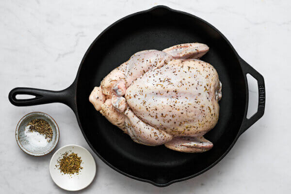 Whole roasted chicken in a skillet next to spices