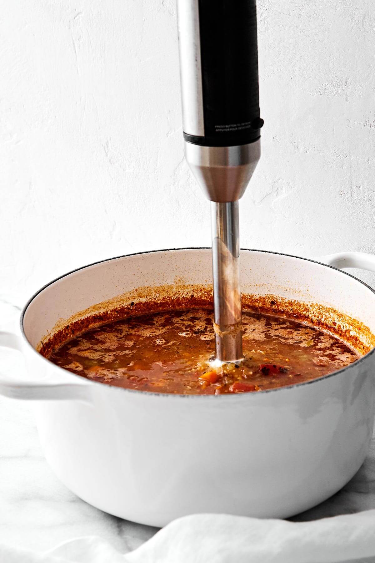 Blending lentil soup in a pot with immersion blender.