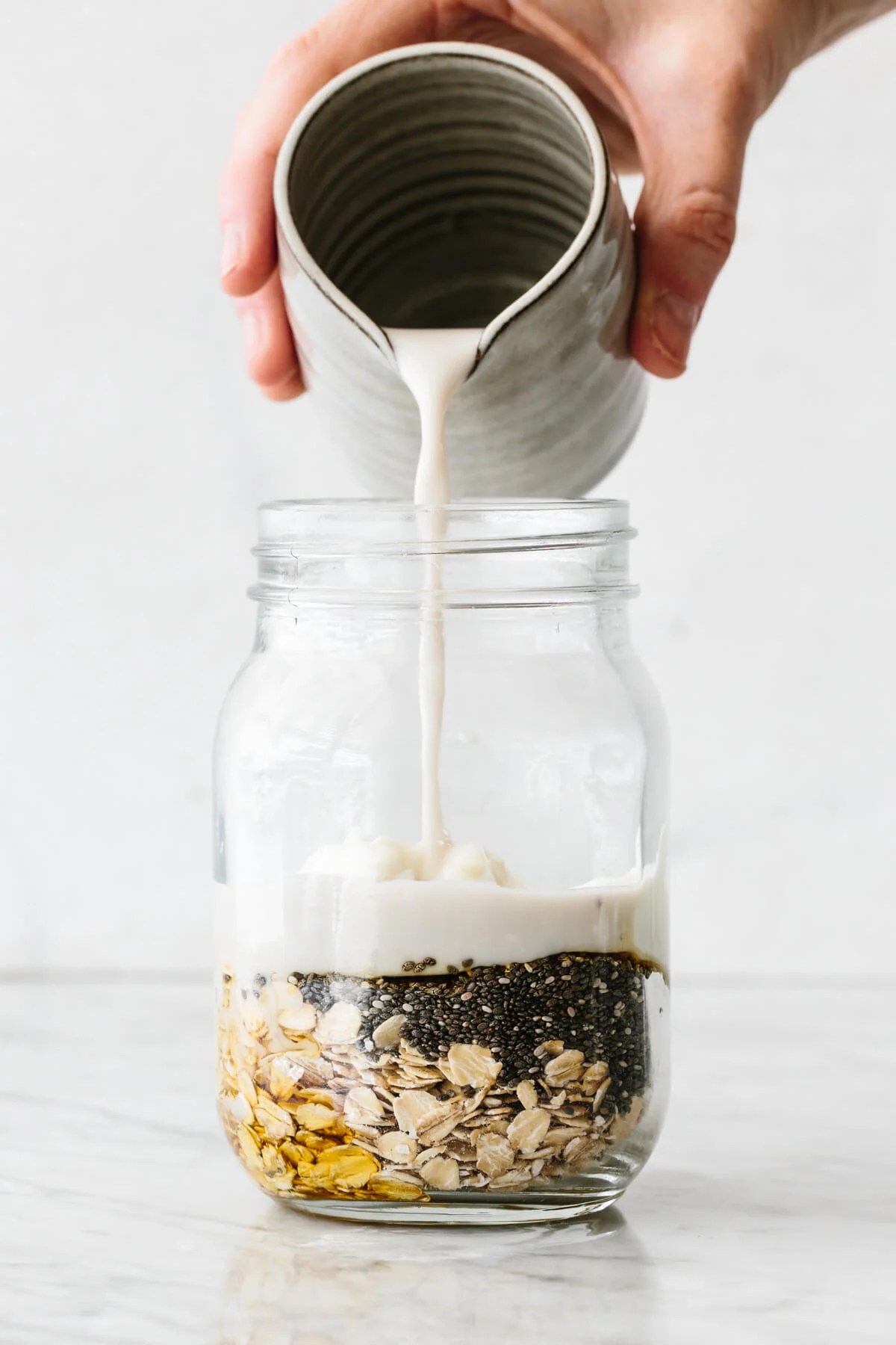 Pouring milk into a jar with overnight oats ingredients.