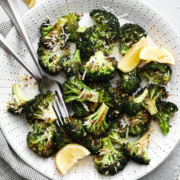 A white plate of roasted broccoli, parmesan, and garlic.