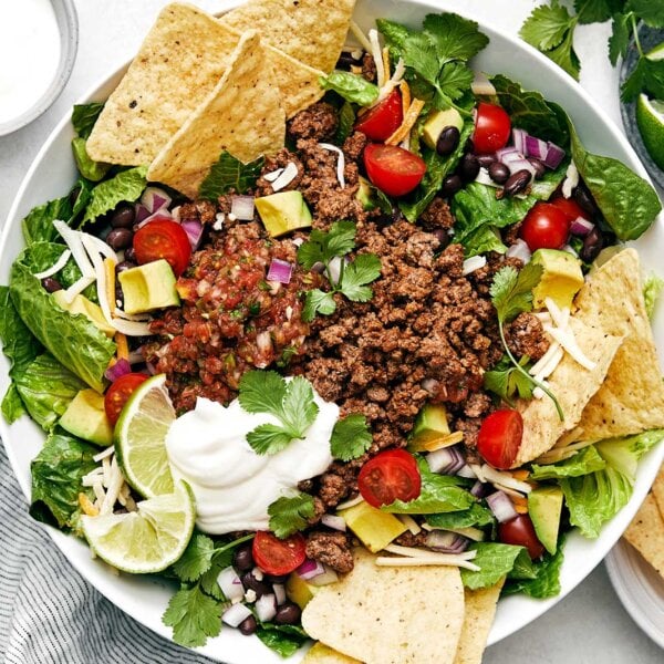 A white bowl of taco salad next to limes.