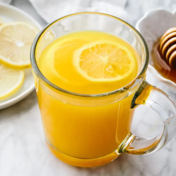 Turmeric tea in a glass with honey and lemon slices in the background.